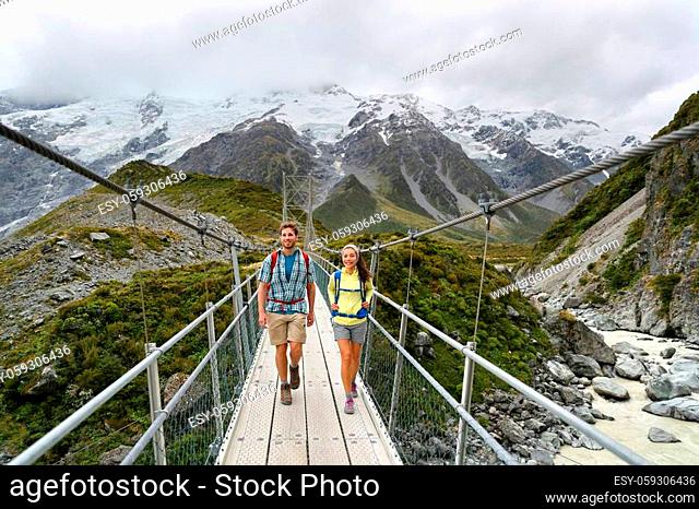 Tourists walking crossing bridge on the Hooker Valley Track hiking trail, New Zealand. Hikers people at Aoraki, Mt Cook National Park with snow capped mountains...