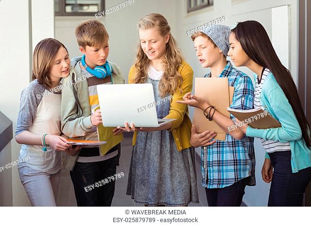 Smiling school students using laptop in corridor