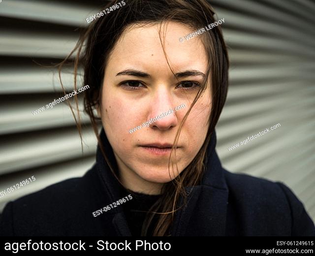 Outdoor portrait of a 28 year old white woman with brown hair posing against an Industrial wall, Brussels, Belgium