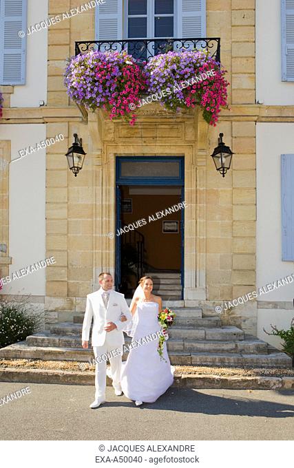 Bride and bridegroom in white dress happily walking out of the registrar's office walking arm in arm