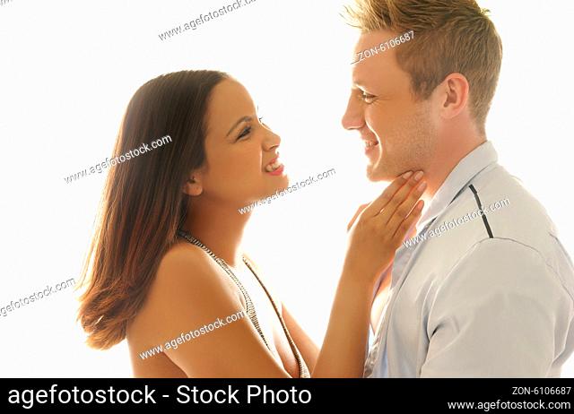 Tenderness and love as a beautiful young woman caresses the throat of her lover while smiling lovingly into his eyes, couple in profile over white