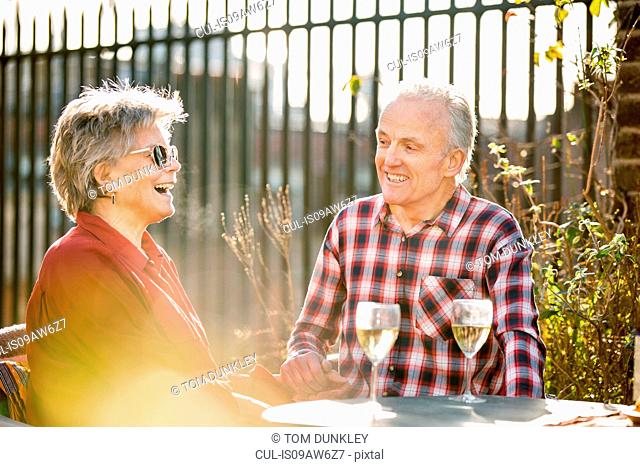Senior couple on rooftop garden chatting and relaxing with white wine