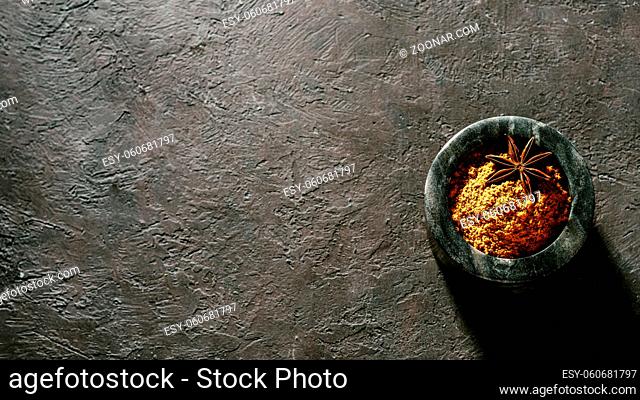 Indian or pakistani masala powder in black marble bowl on black textured background. Small marble bowl with dry curry garam masala mix spices blend with copy...