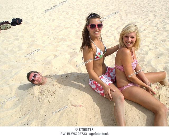 fun at the beach, women sitting on man buried in the sand, Australia, New South Wales