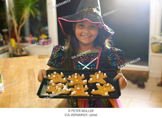 Girl wearing halloween witch costume holding tray of gingerbread men