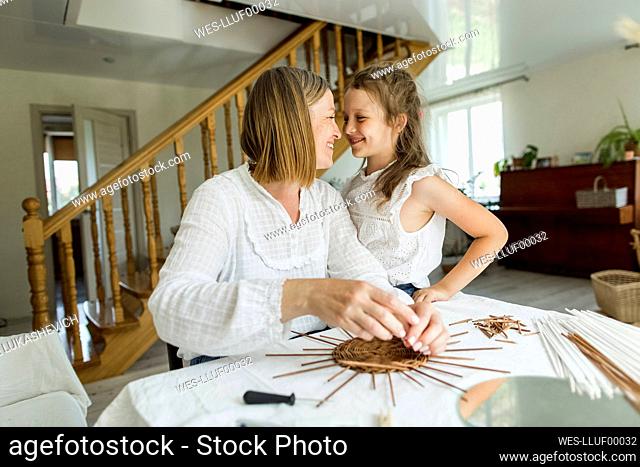 Woman smiling at daughter while weaving basket in living room