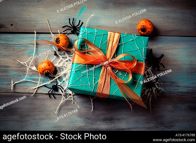 An halloween gift with black spider, orange pumpkin and black stapes. Halloween background, gift on a wood floor