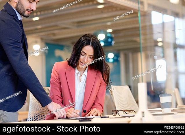 Businesswoman signing contract by male entrepreneur in coworking office