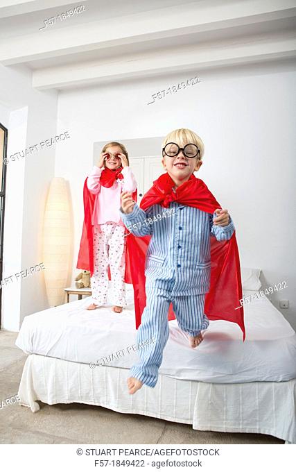 Four year old boy jumping off the bed in a red cape