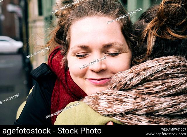 Smiling woman with eyes closed embracing female friend