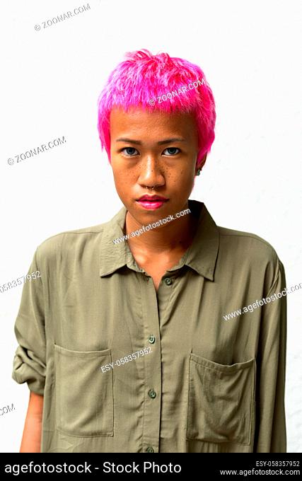 Portrait of young rebellious Asian woman with pink hair against white background