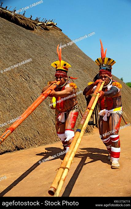 Two native indios with a young girl in festive clothing and feathres in their hair playing their long pipe, Mato Grosso, Brazil, South America