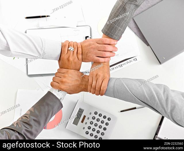 Four hands in unity at businessmeeting in closeup, from high angle view, over table, expressing teamwork