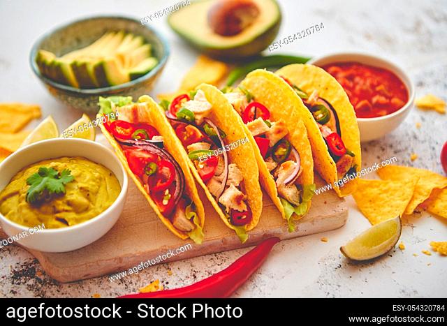 Delicious Mexican fresh crispy tacos are served on wooden board. Stuffed with grilled chicken, spicy pepper, onion, tomato and more