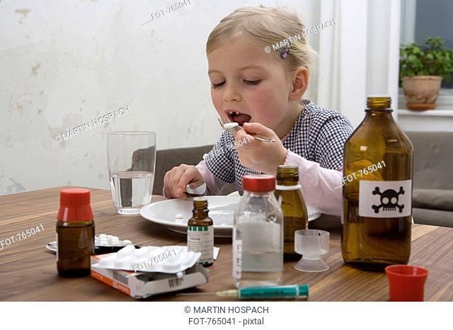 A young girl eating a pill surrounded by medicines