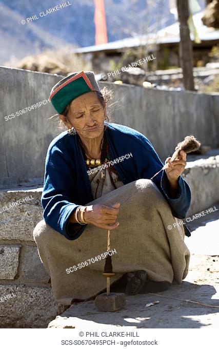 traditionally dressed elderly Kinnauri Buddhist Indian woman concentrating on spinning yarn, Chitkul, Kinnaur valley / district, Himachal Pradesh, Himalayas