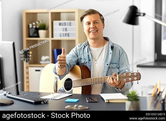 happy man with guitar showing thumbs up at home