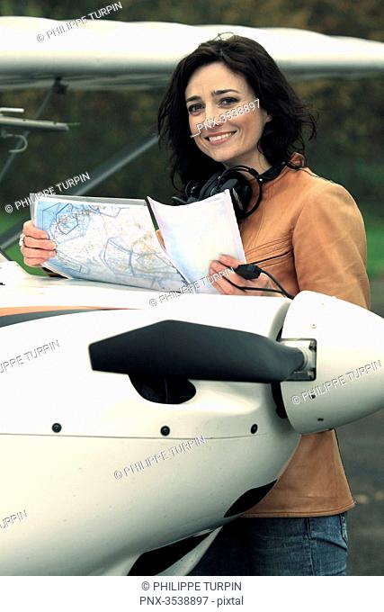 Pilot young woman looking at a map on the hood of her microlight