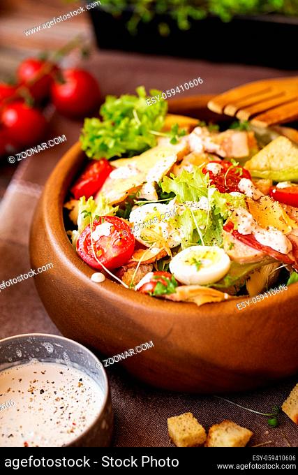 Caesar salad with cherry tomatoes and quail eggs in a wooden bowl