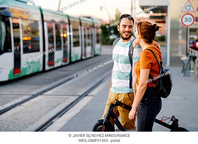 Couple with folded electric scooter waiting at tram stop