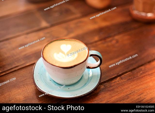 From above of ceramic cup on saucers with freshly brewed latte with hearts on froth