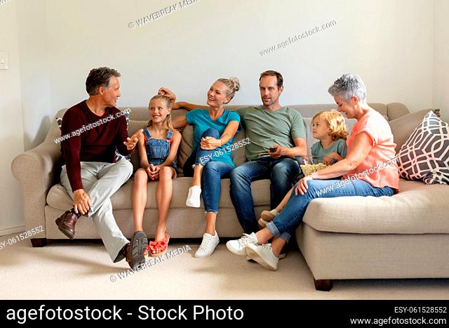 Senior caucasian man sitting on couch talking with his smiling three generation family