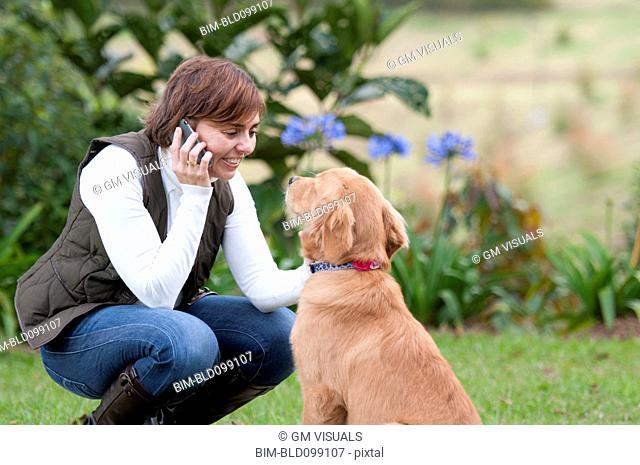 Smiling Hispanic woman talking on cell phone and petting dog