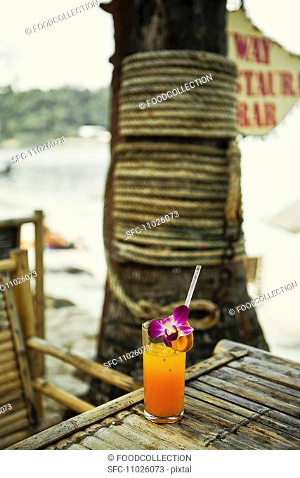 A glass of freshly squeezed orange juice with orchids on a beach Thailand