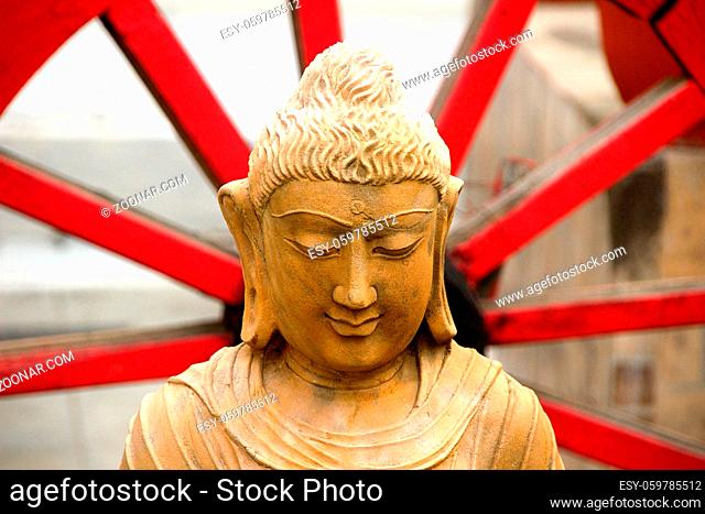 Calm, quiet, wise and serene face of Buddha sitting with red spiked wheel in the background