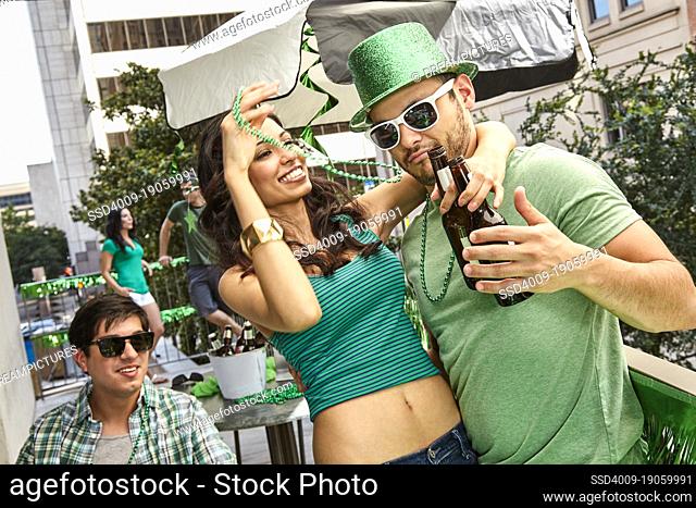 Diverse couple dancing while wearing green at St Patrick's Day party on balcony