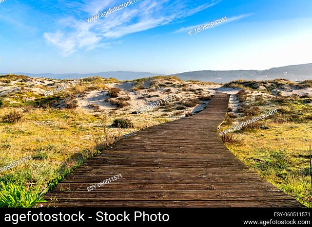 A long wooden boardwalk leading through sand dunes and marsh grass to a beautiful beach