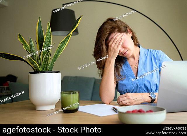 Stressed businesswoman touching forehead and sitting at desk in home office