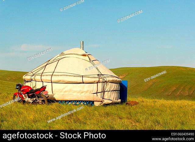 Tent in Mongolian steppes ( namely 'yurt' ) and parked motorcycle.Nowadays it is an alternative to the horses