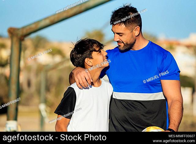 Smiling father with arm around neck of son at sports court