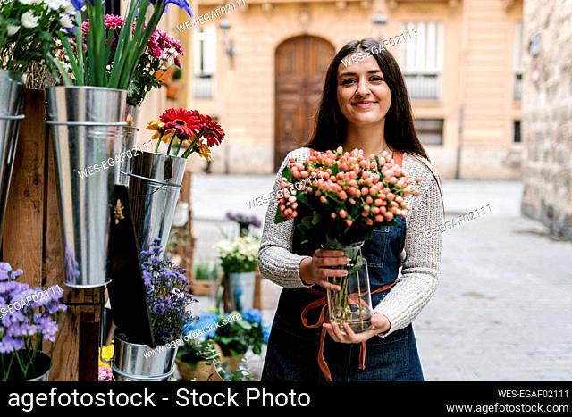 Young female florist holding Hypericum flower vase while standing at flower shop