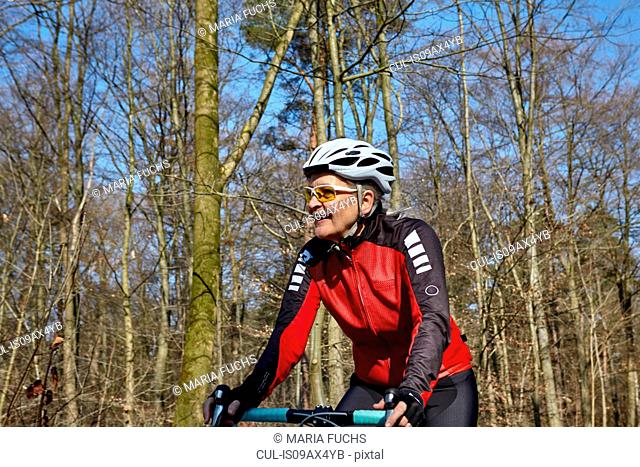 Woman wearing cycling helmet and sunglasses cycling, looking away smiling
