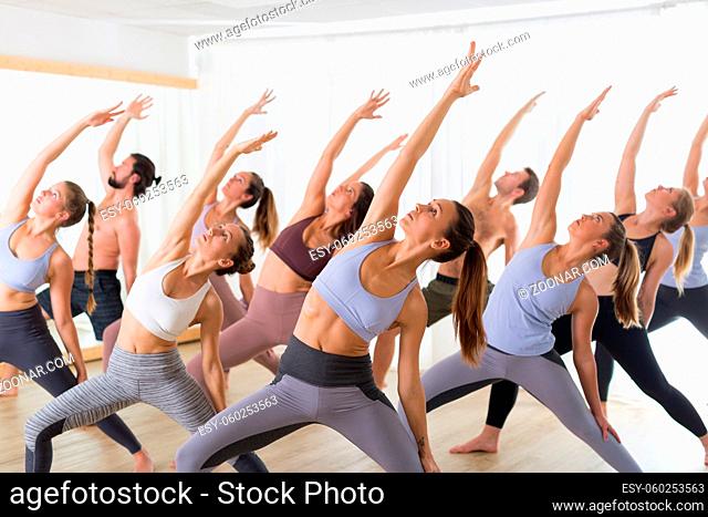 Group of young sporty attractive people in yoga studio, practicing yoga lesson with instructor, sitting on floor in Padmasana, lotus meditative yoga pose