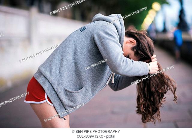 Young female runner tying up long hair on riverside