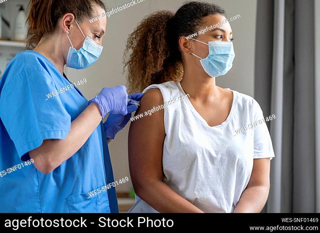 Curly haired woman with face mask getting vaccinated at hospital