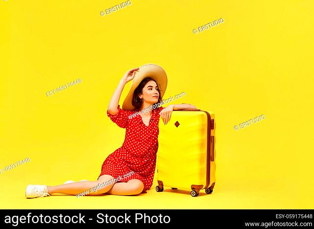 Happy woman in red dress with suitcase going traveling on yellow background. concept of travel. copy space