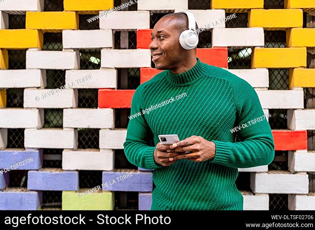 Smiling man listening music through wireless headphones in front of multi colored wall