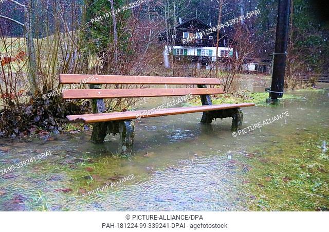 24 December 2018, Bavaria, Fischen: A park bench stands in Fischen (Bavaria) on a flooded meadow. After heavy rain and thaw