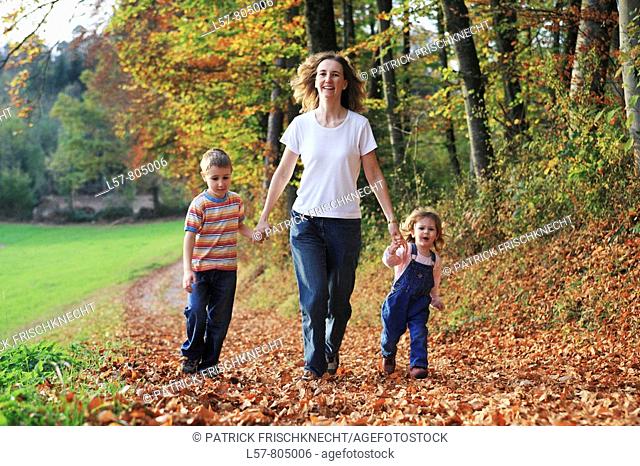 Mother with daughter and son running hand in hand on path full of leaves in fall, having fun and laughing, autumn foliage covering path in forest, autumn, fall