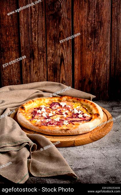 Pizza with ham, cheese and cottage cheese lies on a gray concrete table near a piece of cloth. Italian cuisine