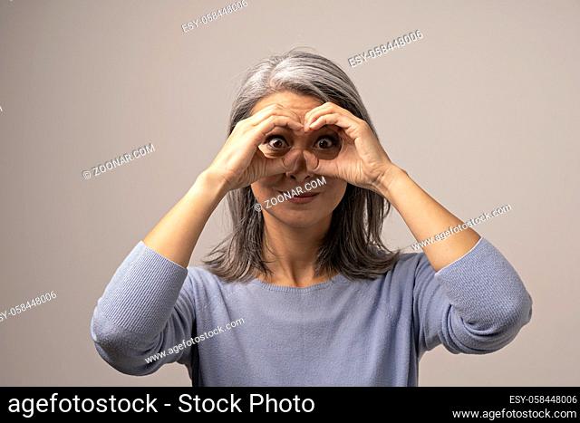 Charming Woman Does Glasses With Her Hands And Looks With Her Eyes Wide Opened At Camera. Middle-Aged Woman Has Fun And Looks Thought Her Hands