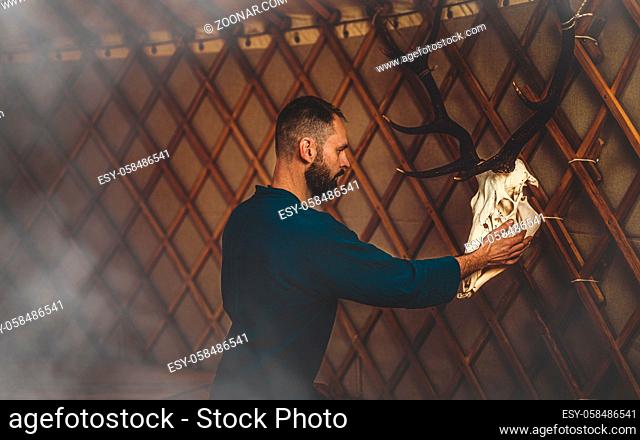 beautiful shamanic man with deer skull in yurt
