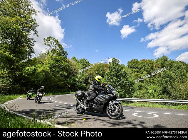 17 May 2023, North Rhine-Westphalia, Hürtgenwald: Motorcyclists drive through a switchback with painted circles on the roadway near Vossenack