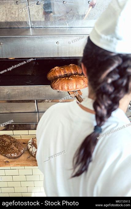 Baker woman getting fresh bread with shovel out of oven