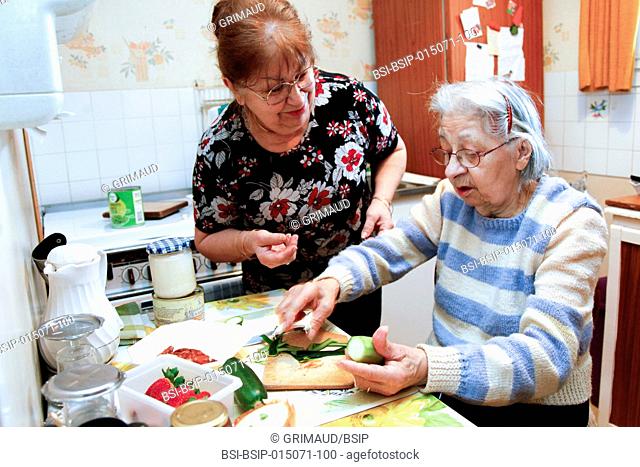 An elderly woman cooking in her home, helped by her daughter who is her guardian