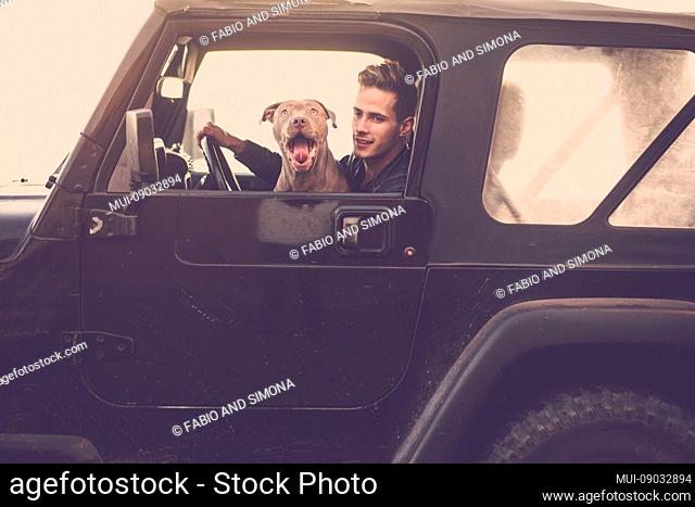 Couple of crazy funny friends driving black car together: man and shouting hungry dog traveling with off road vehicle - vintage filter and brown colors for...